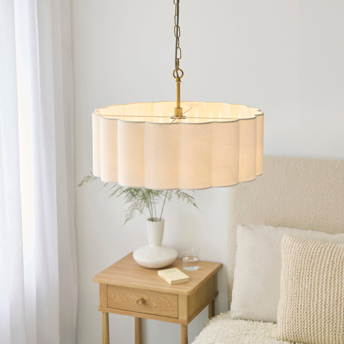 Serene pendant glowing above an oak bedside table with vase, book and cream cushions