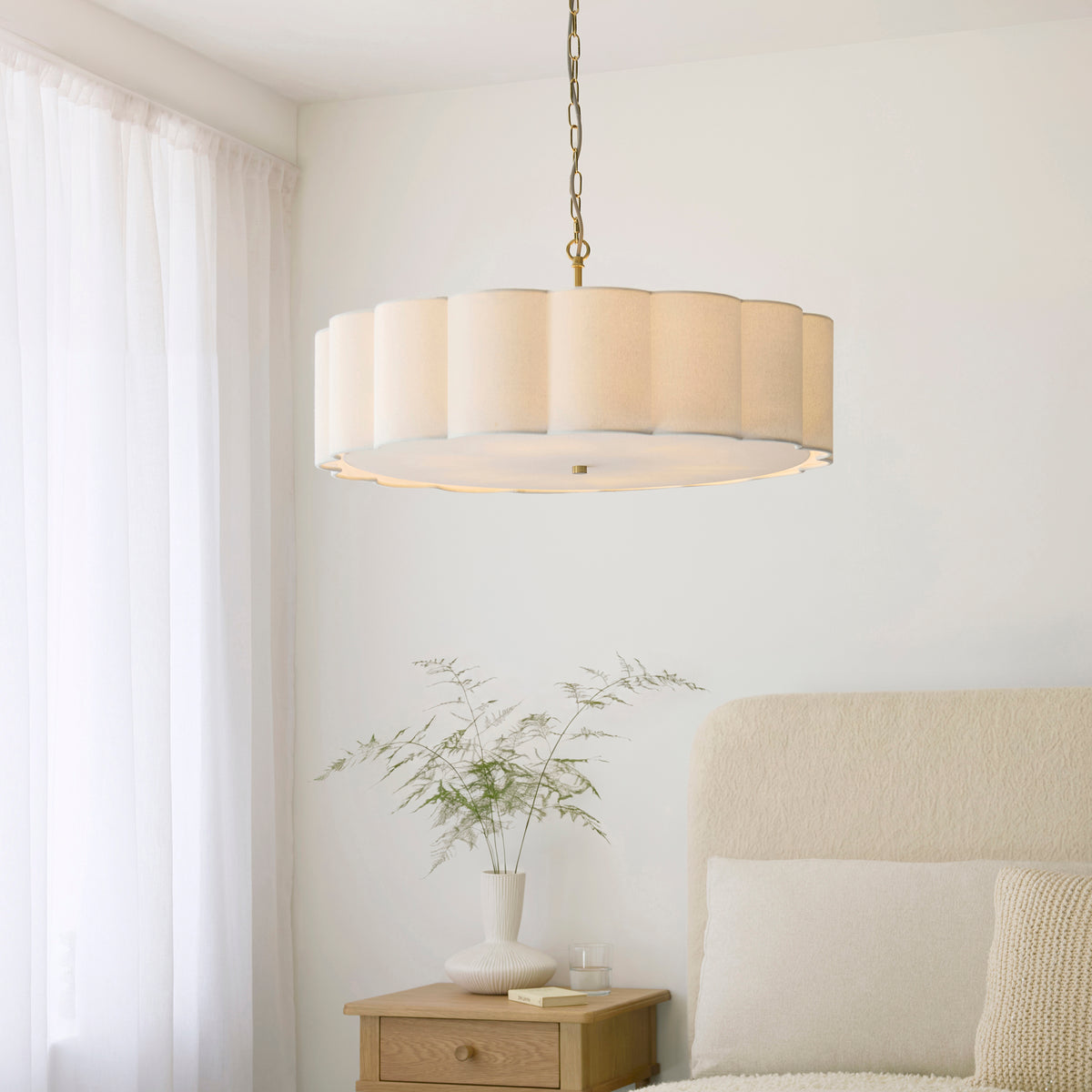 Wide scalloped cream chandelier glowing in a bedroom with oak bedside table and boucle headboard