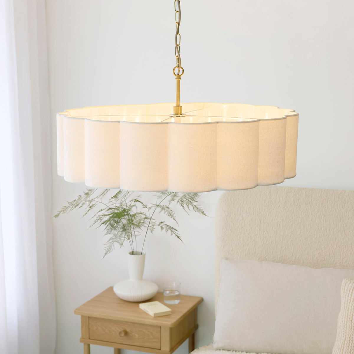 Serene chandelier seen from below, scalloped cream shade lit above a styled bedside table
