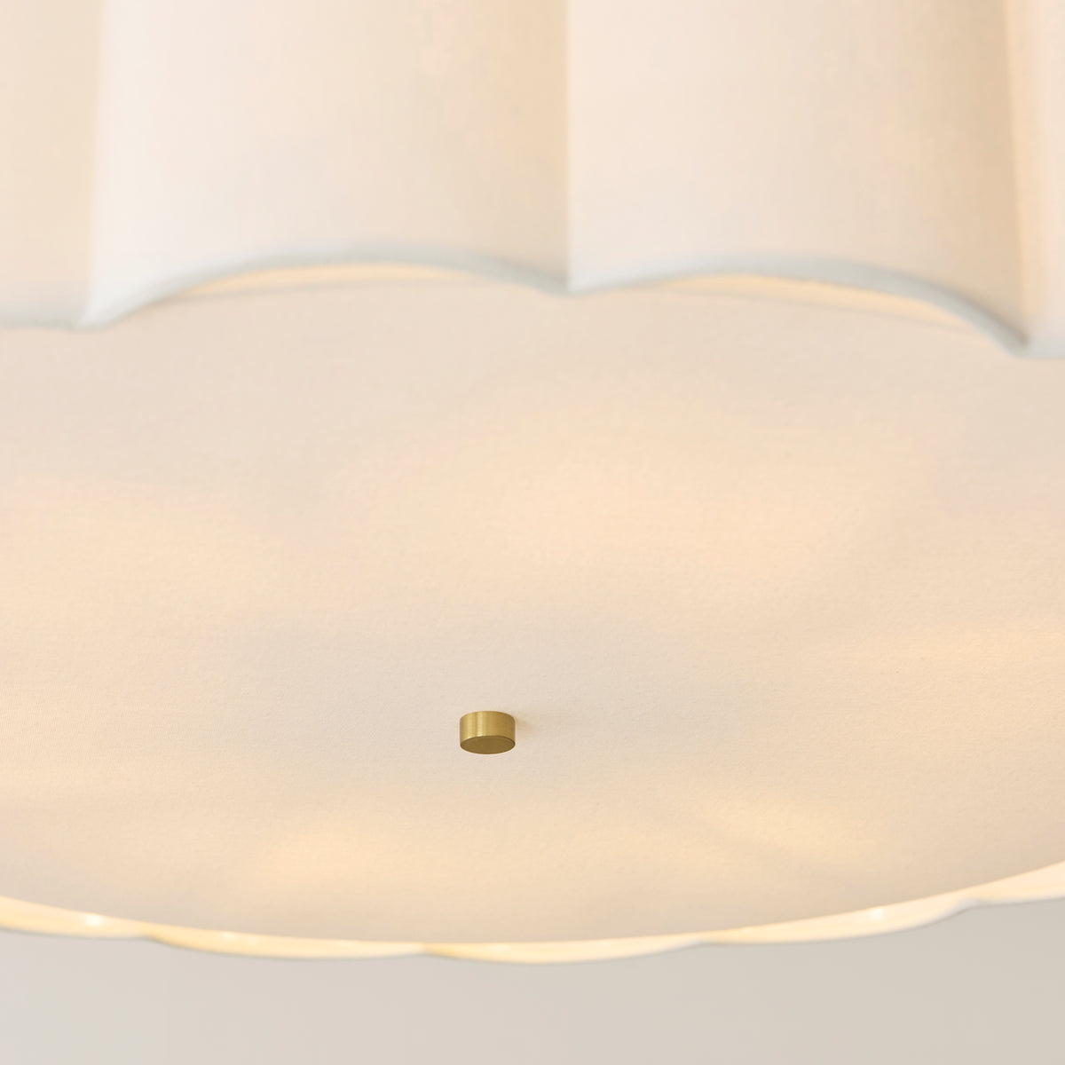Detail of the glowing fabric diffuser and small brass finial beneath the scalloped shade