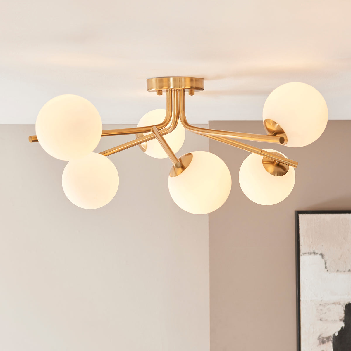 Aaron brushed aged brass semi flush light on a white ceiling above a framed monochrome print