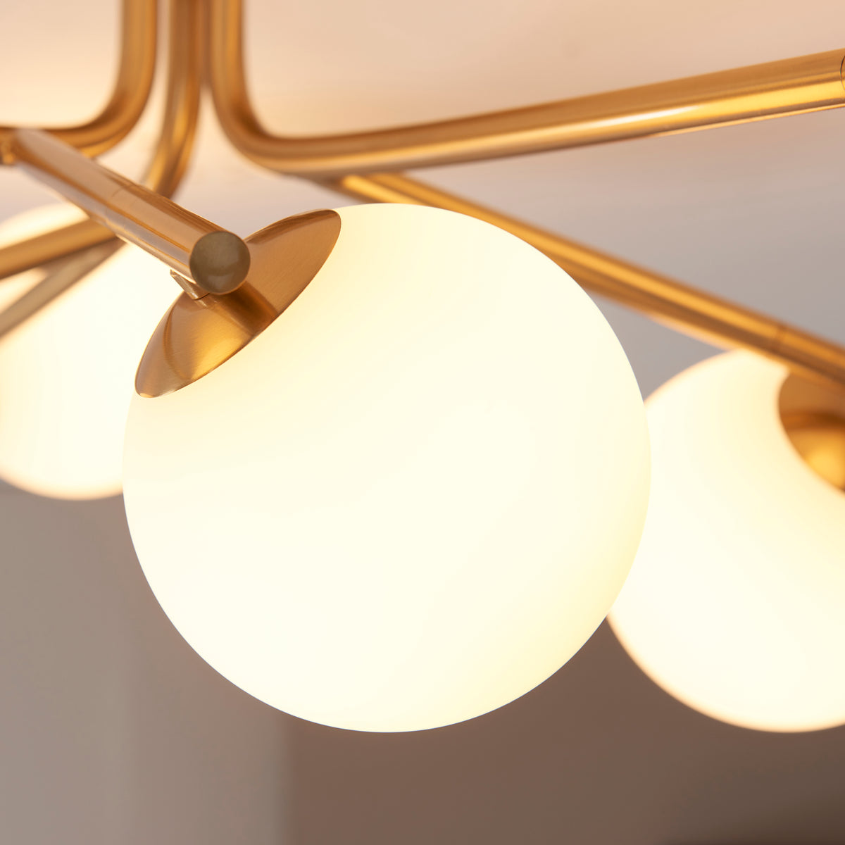 Close-up of a glowing opal glass globe and brushed brass cup on the Aaron semi flush light