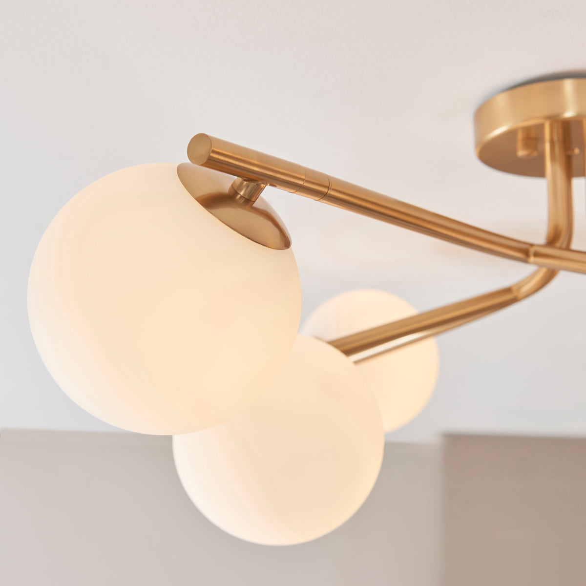 Detail of three opal glass globes clustered on the brass arms of the Aaron semi flush light
