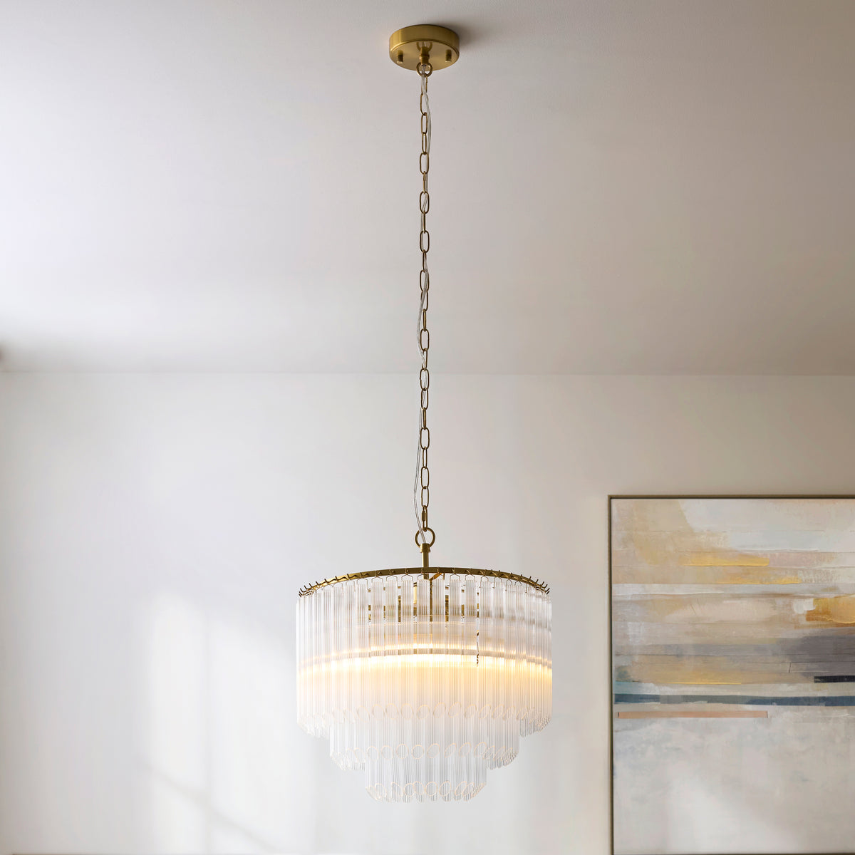 Montpellier aged brass chandelier hanging from a white ceiling beside a pale abstract picture