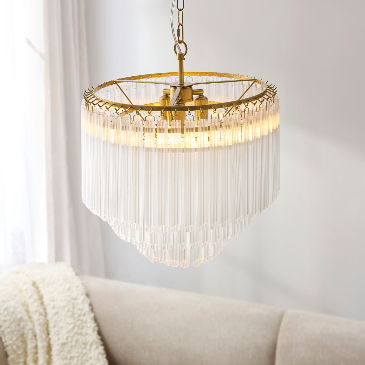 Tiered ribbed glass rods and brass frame of the lit Montpellier chandelier above a sofa