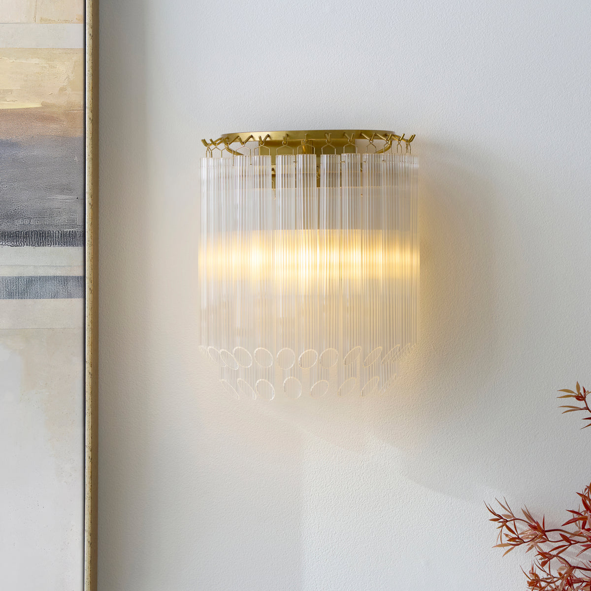 Montpellier ribbed glass wall light glowing on a pale wall beside framed art and red foliage