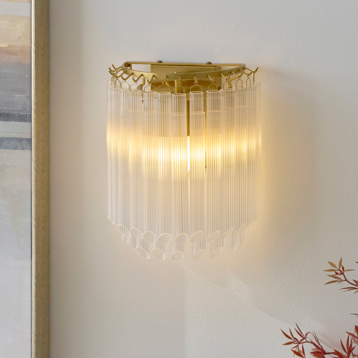 Montpellier ribbed glass wall light illuminated next to a framed picture and dried stems