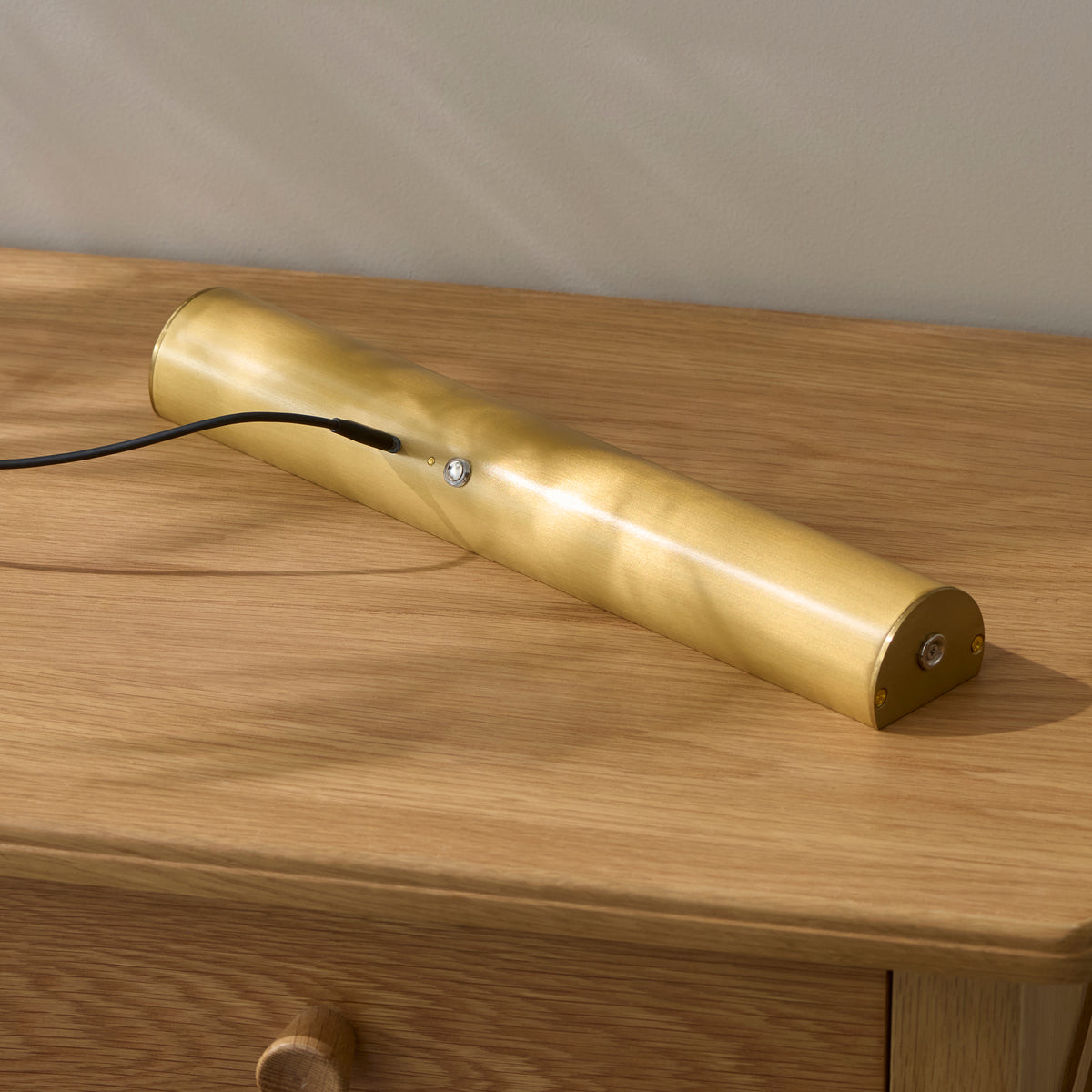 Nantes rechargeable brass picture light lying on an oak surface with its charging cable