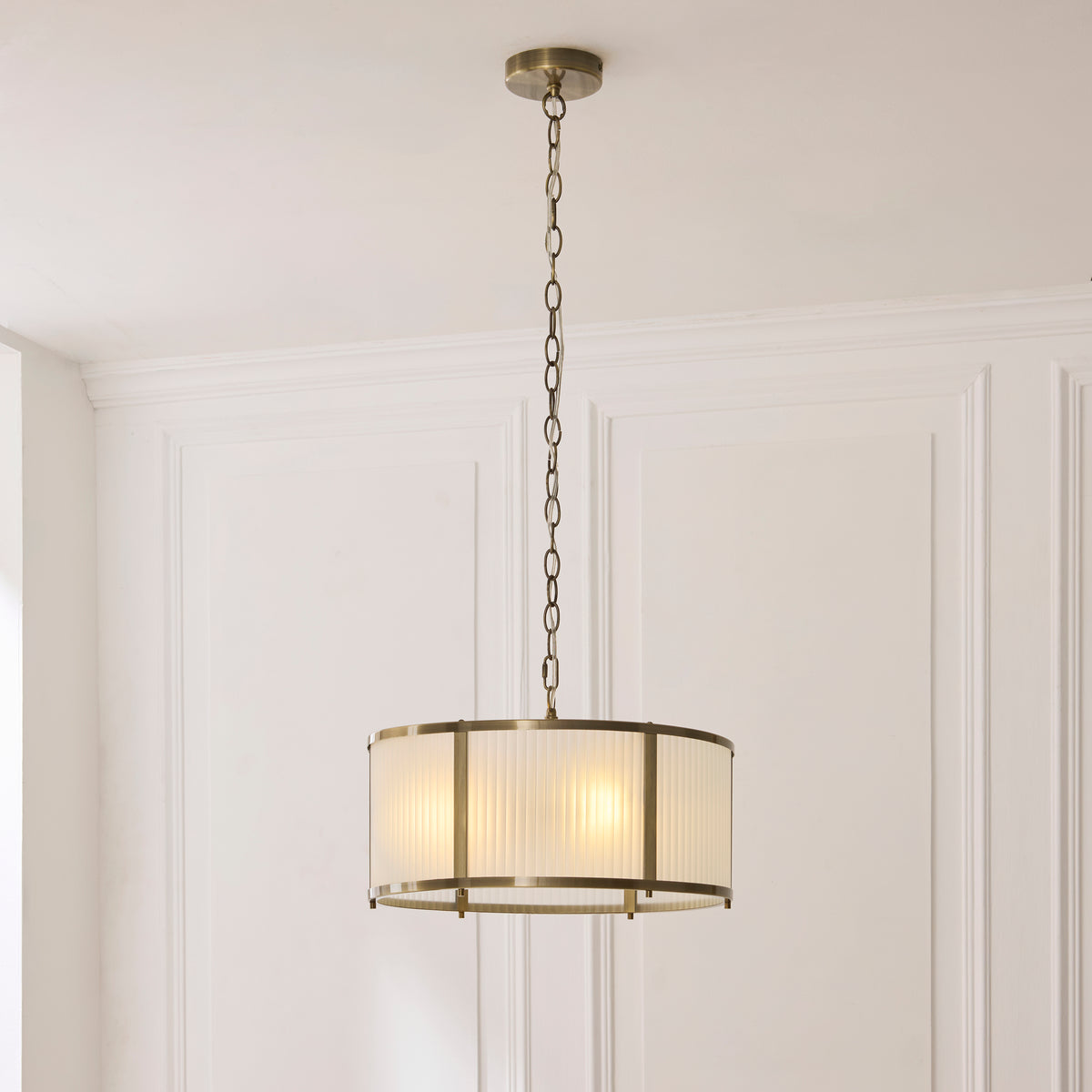Ridgeton antique brass pendant hanging on a long chain against a white panelled wall