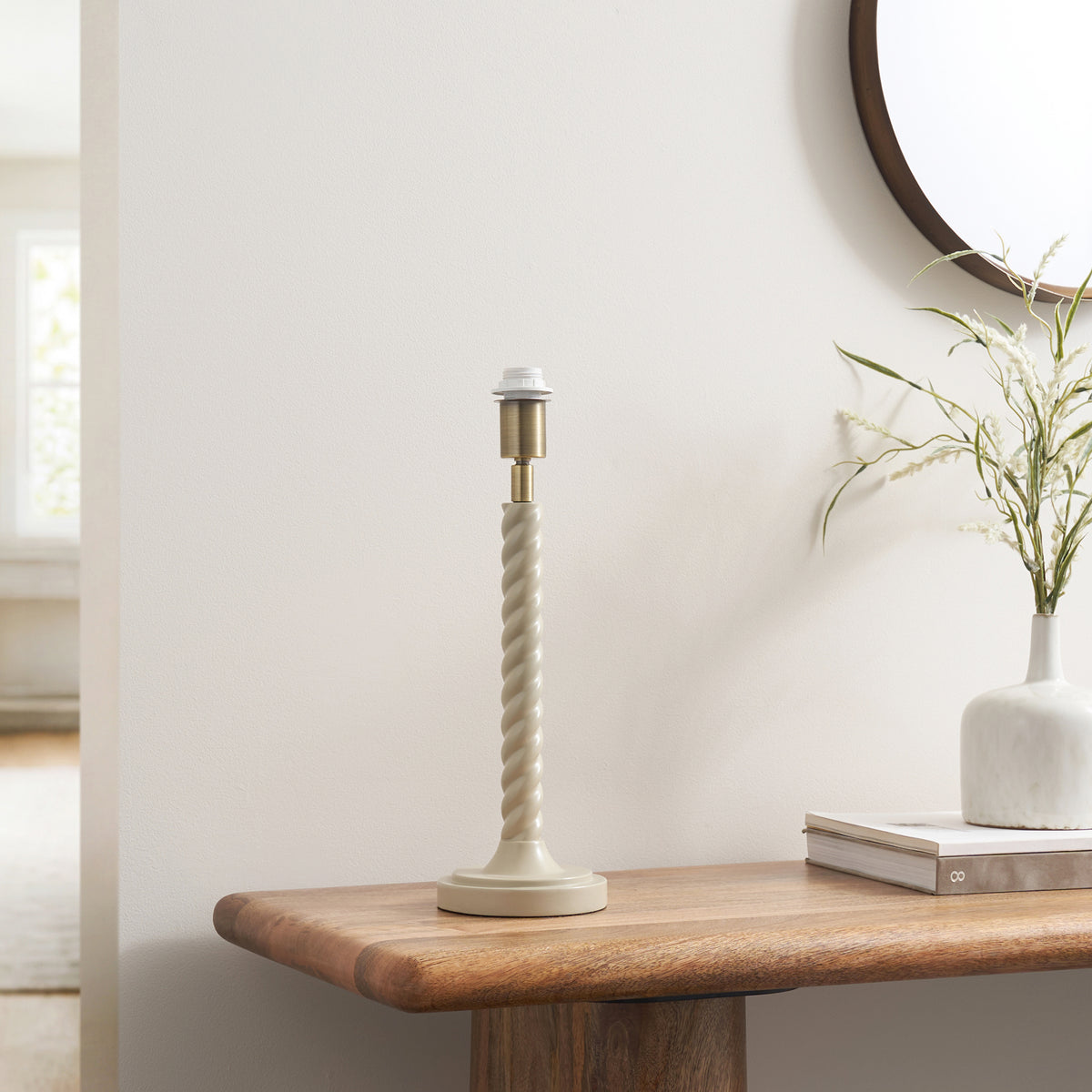 Twist almond white table lamp base on a wooden console with vase and books in a hallway