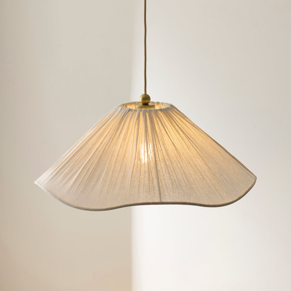 Isabella pendant's wavy pleated cream shade lit from within on a slender flex