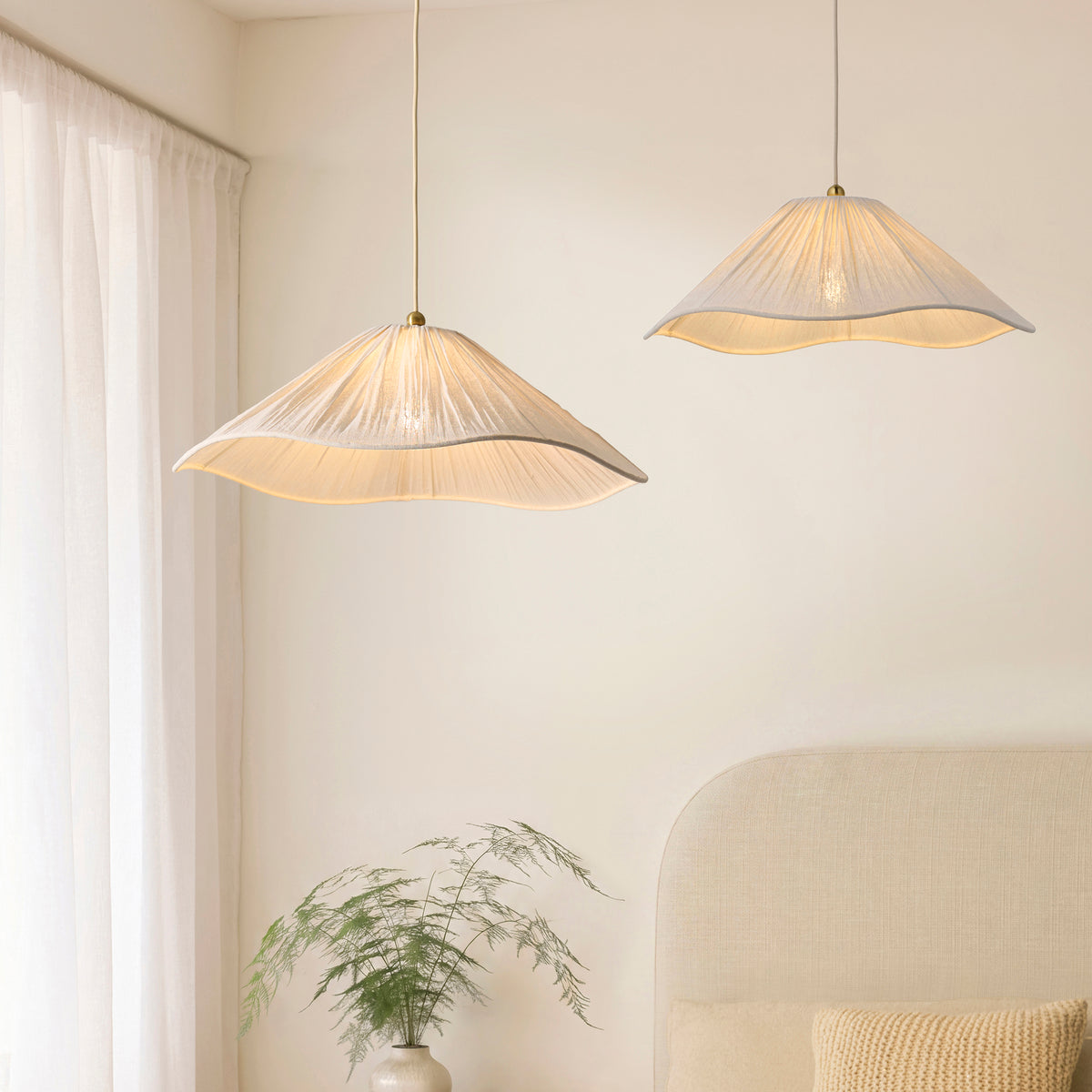 Pair of Isabella pleated white pendants lit above a bed beside curtains and a potted fern