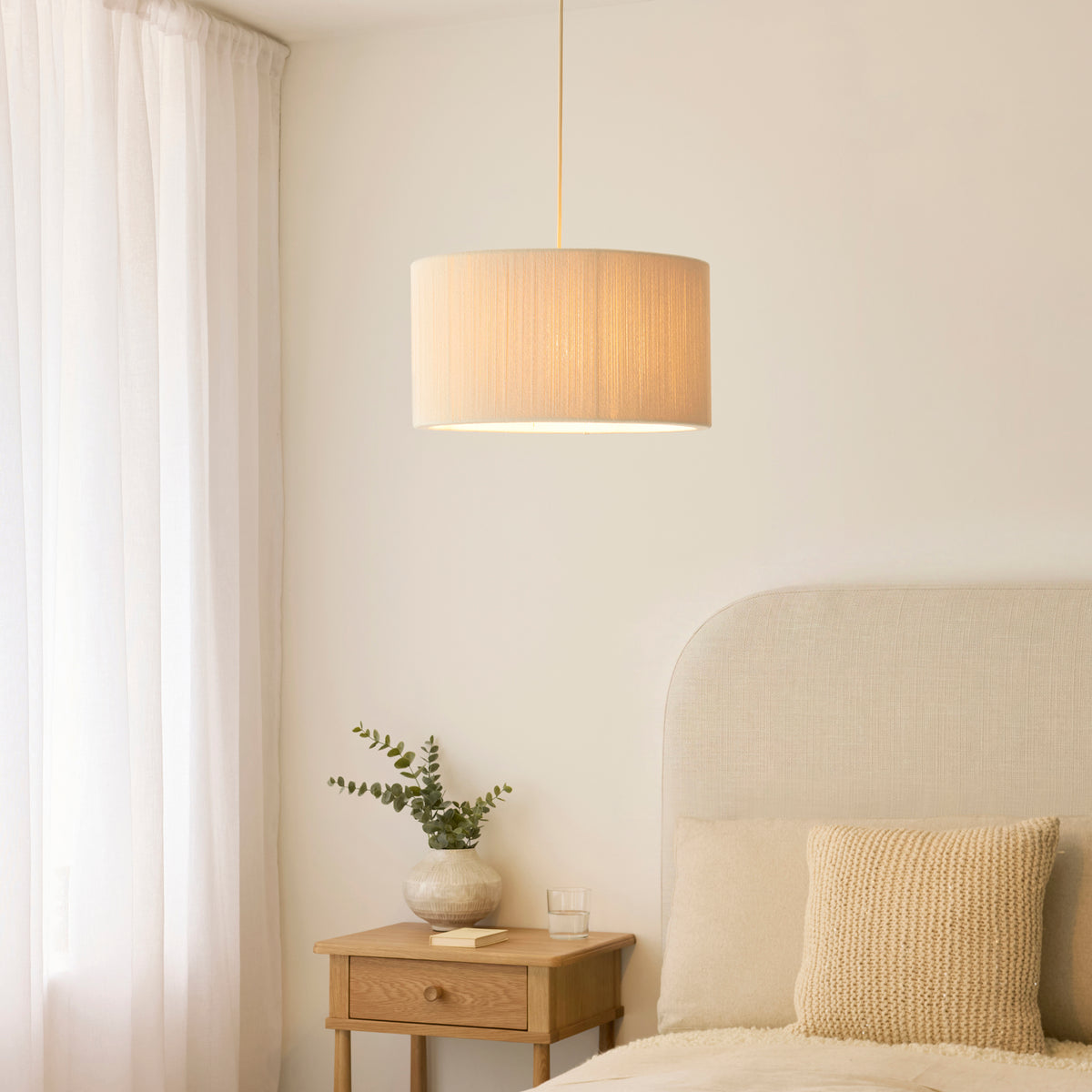 Noah cream pendant lit above an oak bedside table with eucalyptus in a calm bedroom