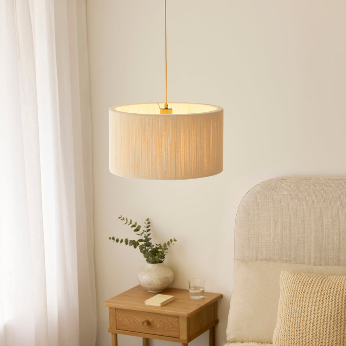 Noah cream drum pendant glowing beside a bed with upholstered headboard and bedside table