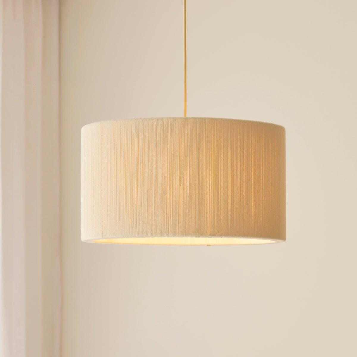Illuminated Noah cream drum shade on a brass suspension against a pale wall