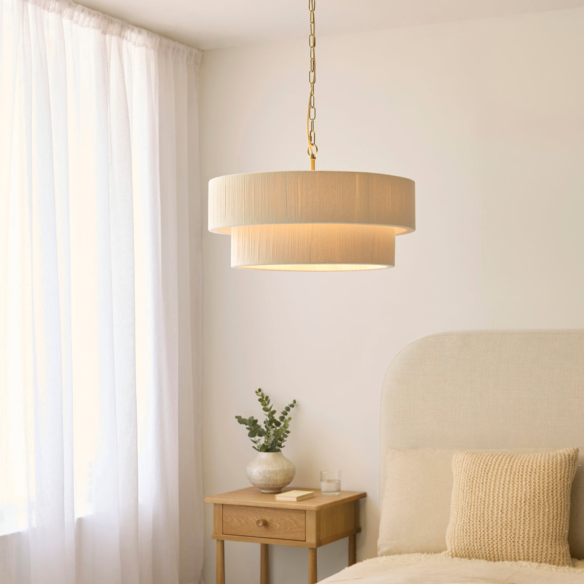 Noah tiered cream pendant lit above an oak bedside table with eucalyptus in a bedroom