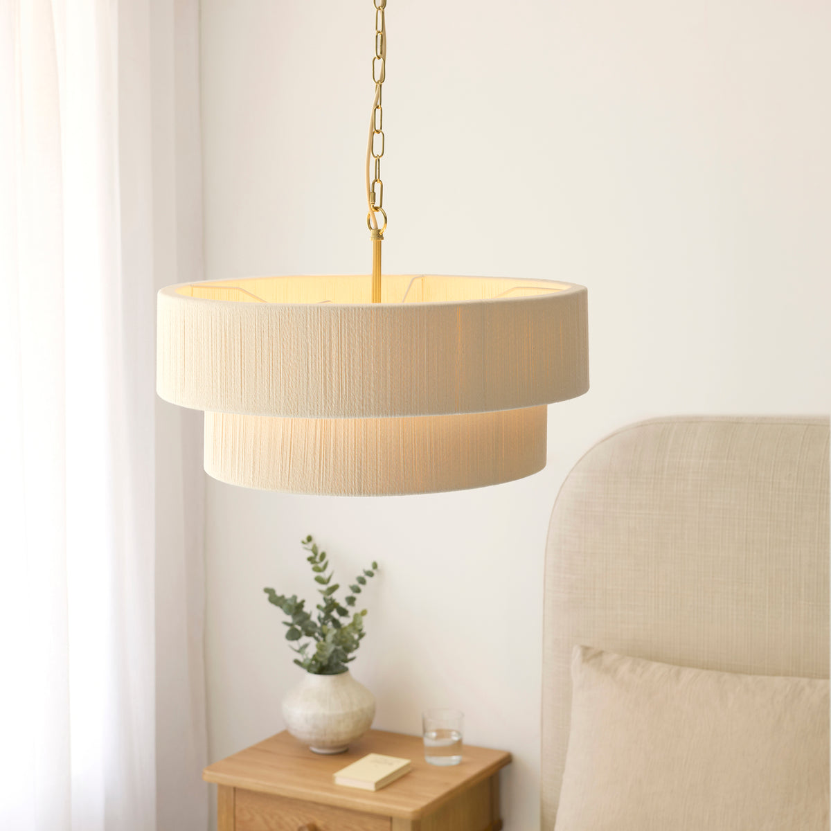 Illuminated Noah two-tier cream pendant beside a bed with fabric headboard and bedside table