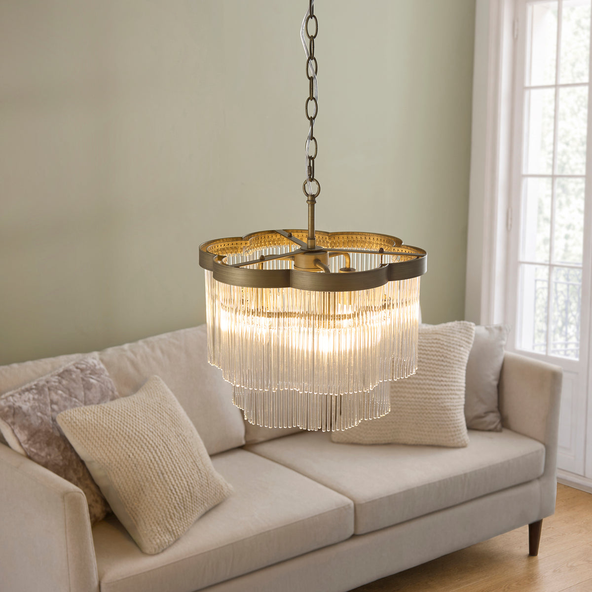 Lucille chandelier glowing above a cream sofa with cushions, seen from below