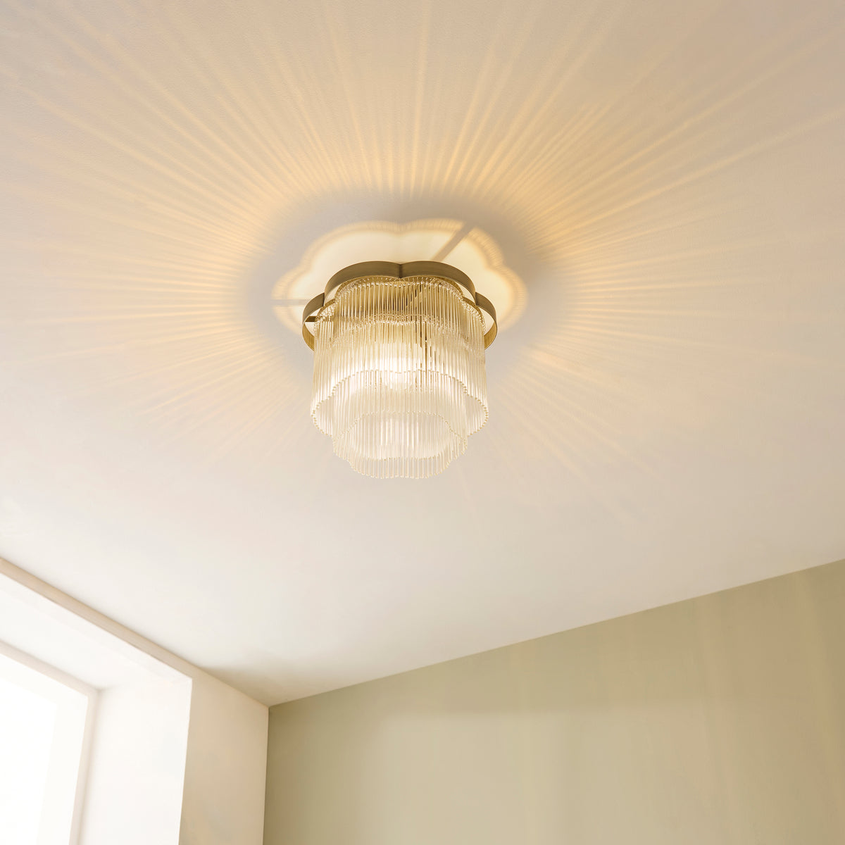 Lucille glass rod flush light glowing on a white ceiling, seen from below with radiating light patterns