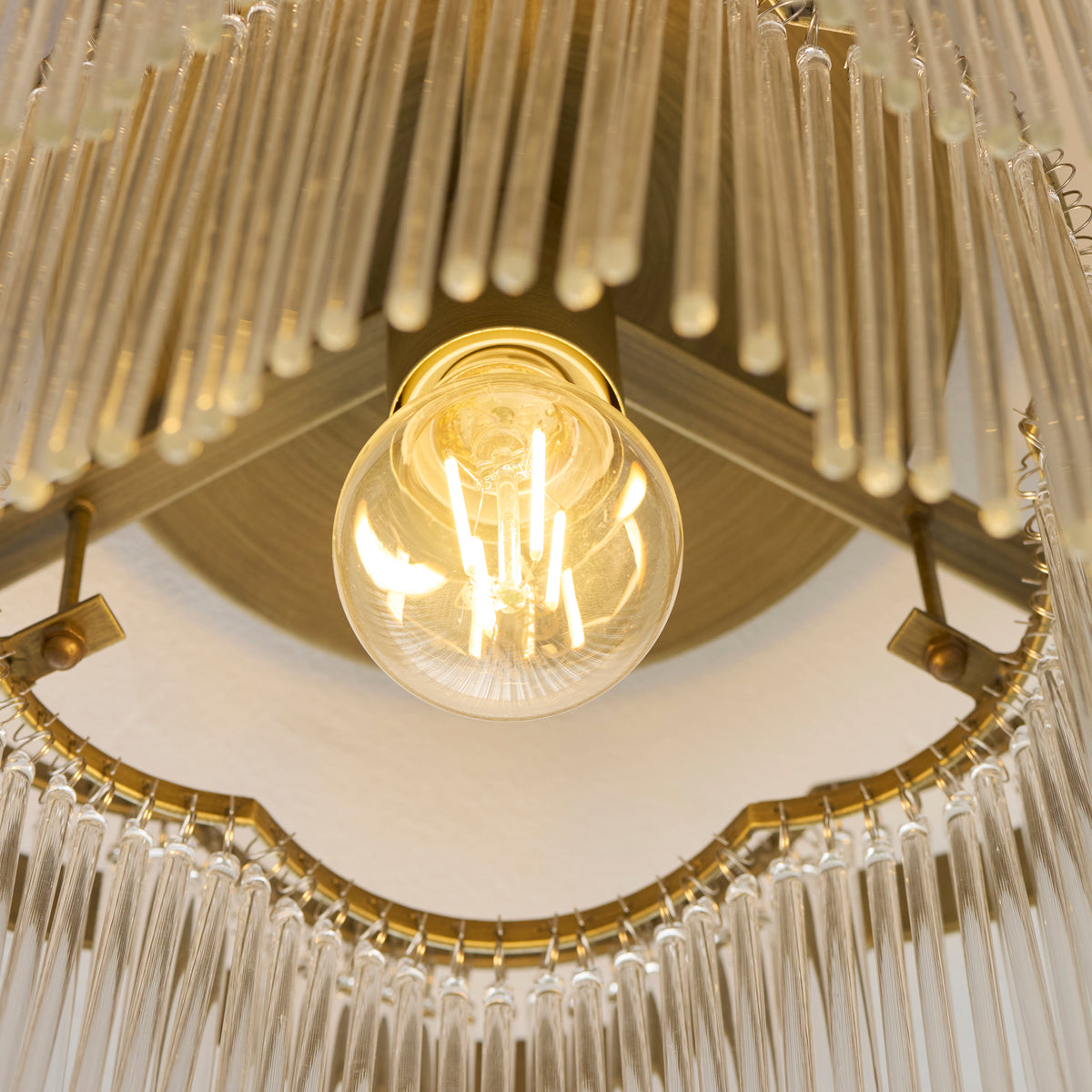 Underside of the Lucille flush light showing the exposed filament bulb within the brass scalloped frame