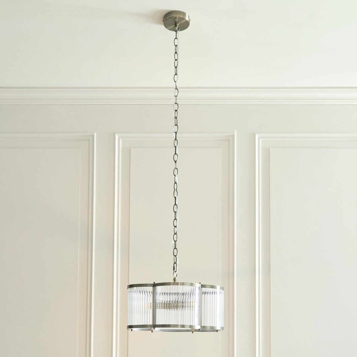 Ridgeton Scallop pendant hanging on a long chain against a panelled cream wall