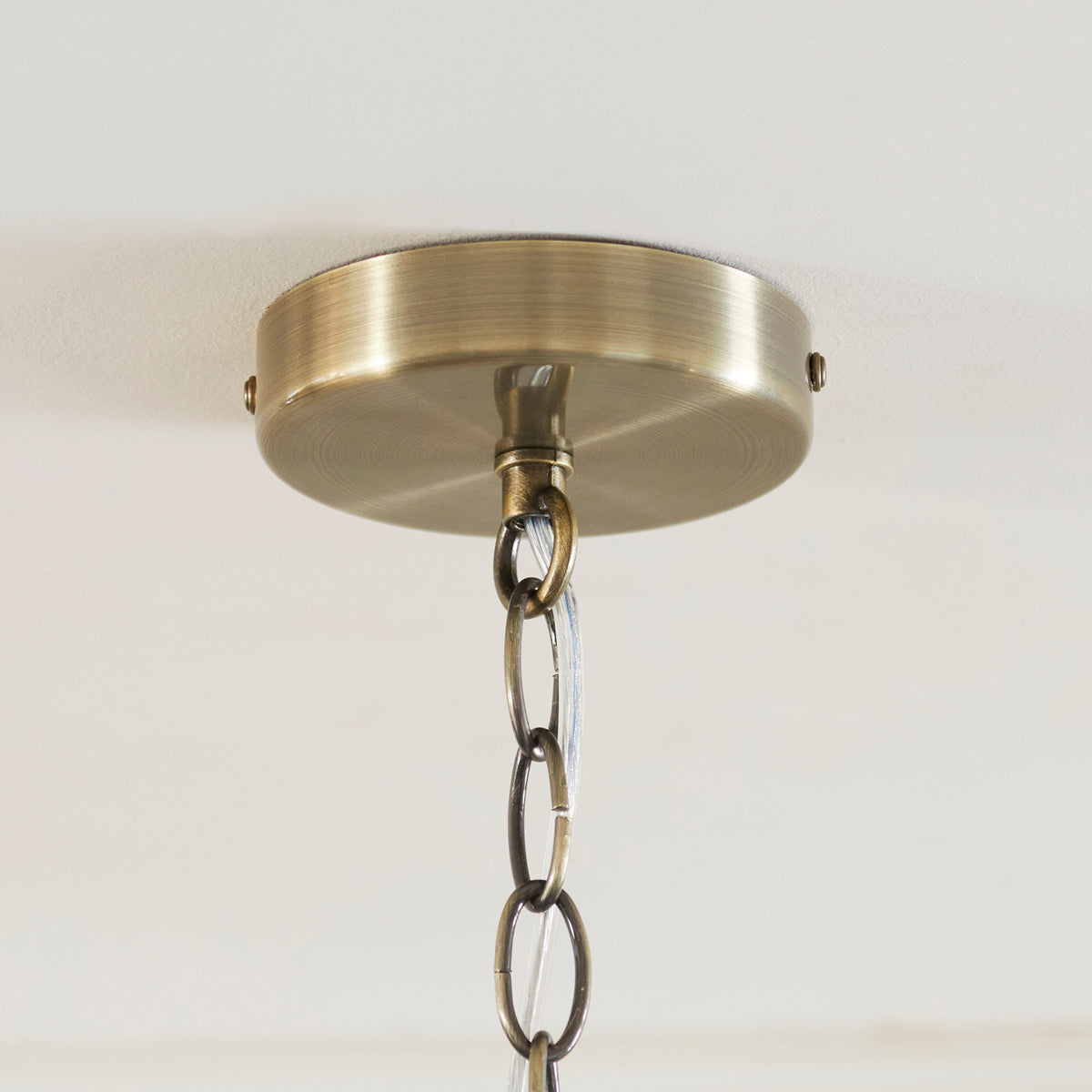 Antique brass ceiling rose and chain detail of the Ridgeton Scallop pendant on a white ceiling