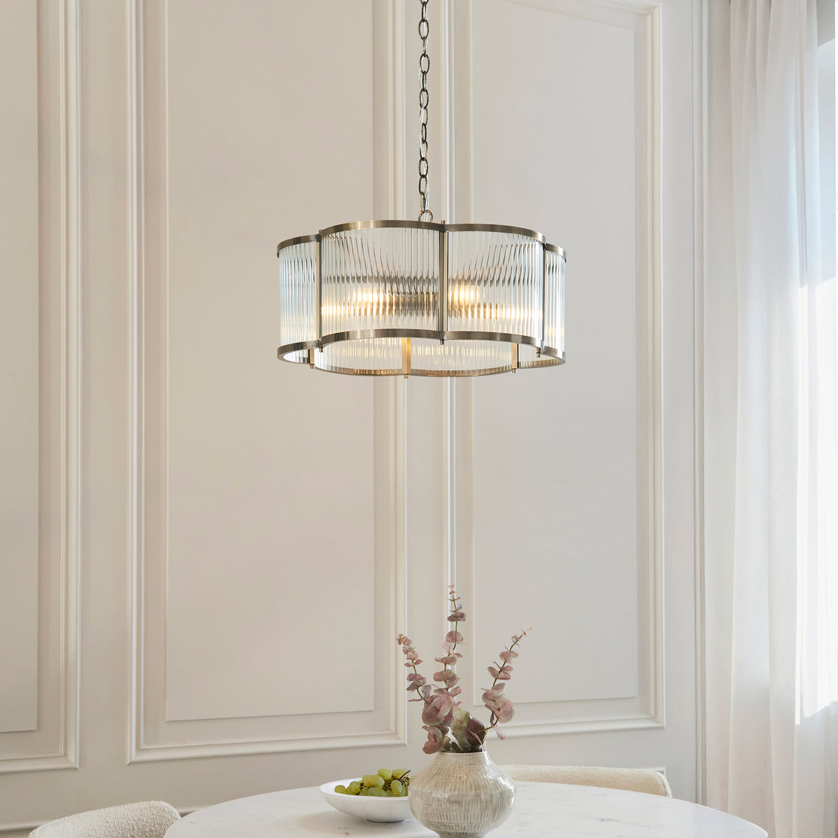 Ridgeton Scallop chandelier lit above a dining table with fruit bowl and flowers by a curtained window