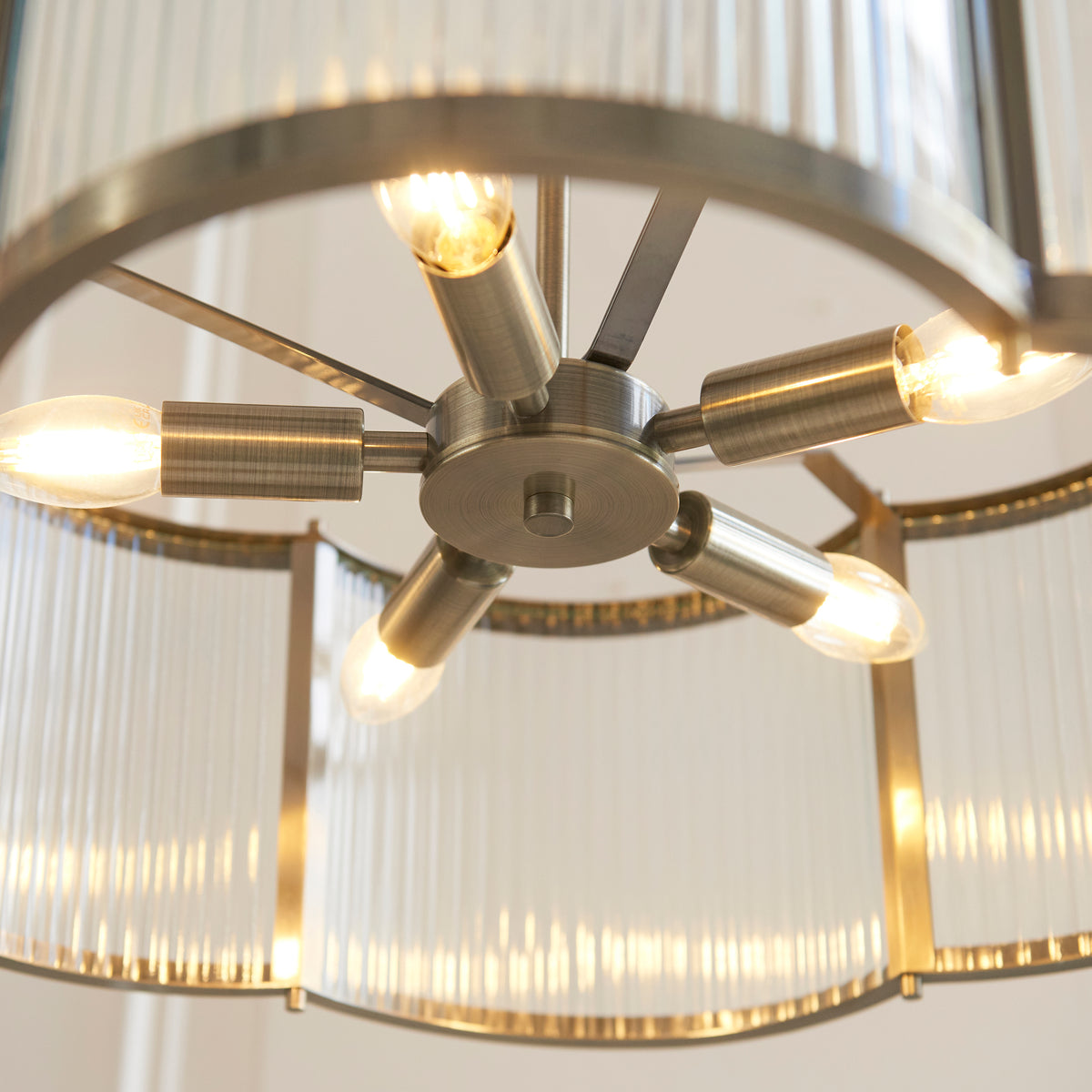 Close-up of the chandelier's antique brass arms and lit candle bulbs behind ribbed glass
