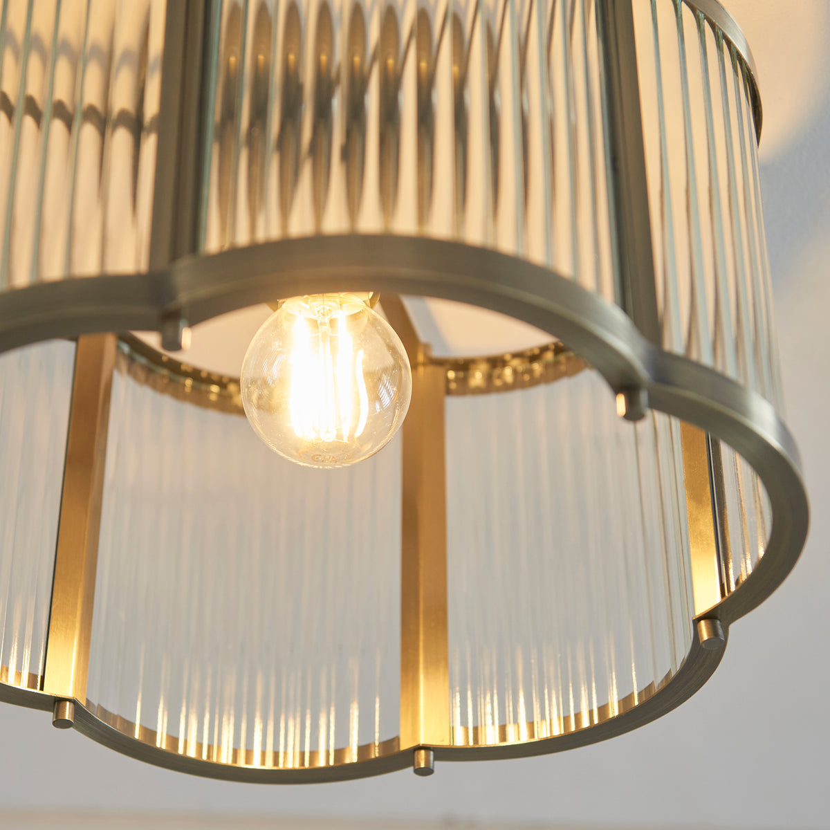 Close-up of the lit bulb inside the Ridgeton Scallop light's ribbed glass and antique brass frame