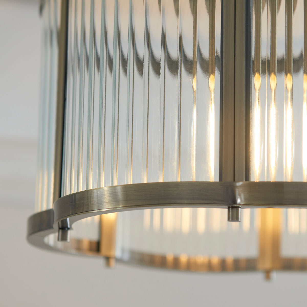 Close detail of ribbed glass panels glowing behind the brushed antique brass band of the Ridgeton light