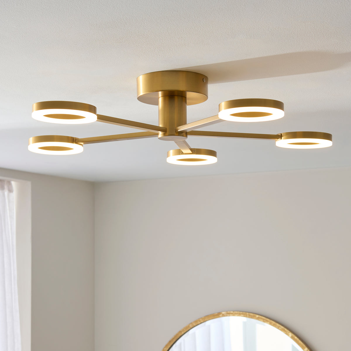 Scout warm brass semi-flush light glowing on a bedroom ceiling above a round mirror
