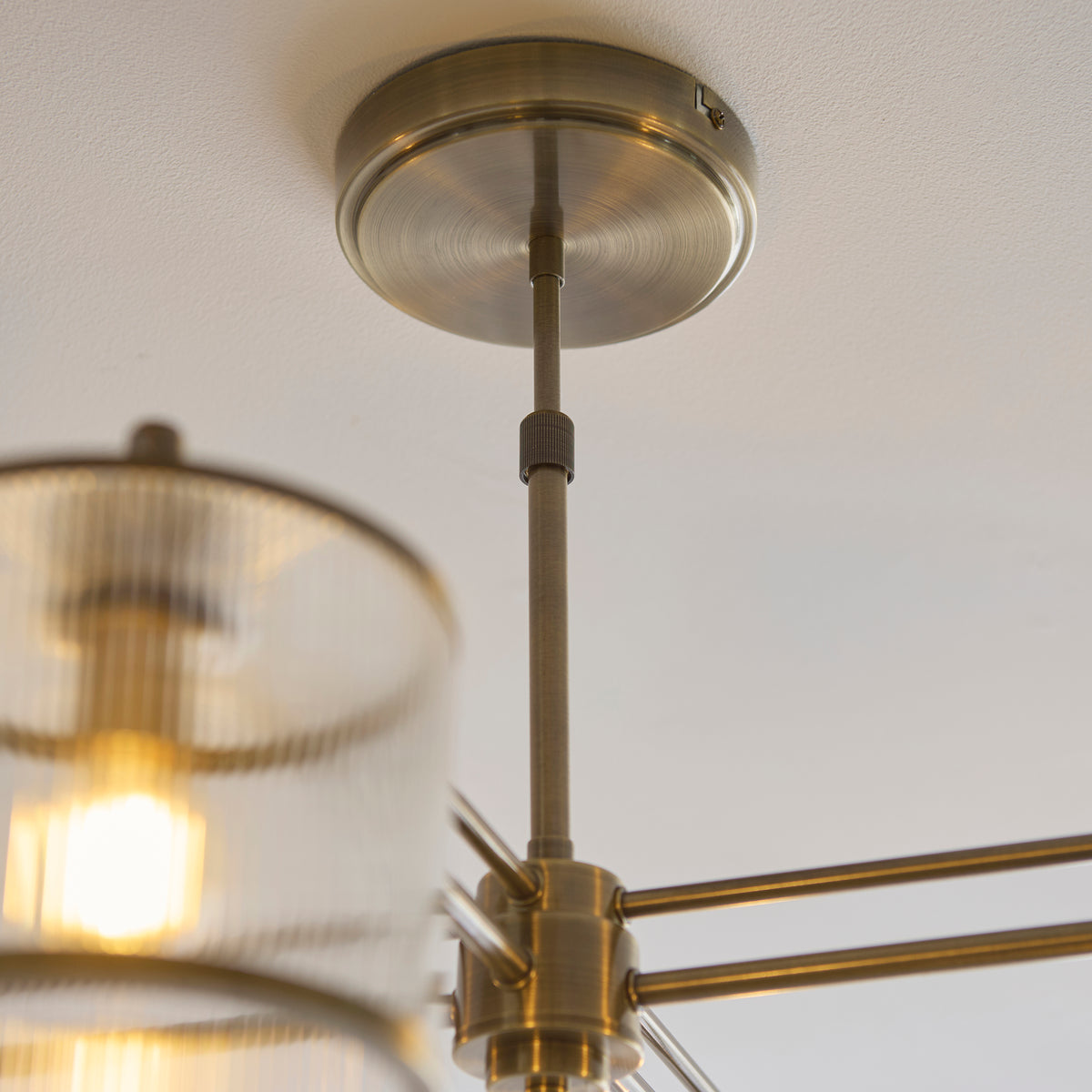 Antique brass ceiling rose and stem of the Ridgeton chandelier with a lit ribbed glass shade below
