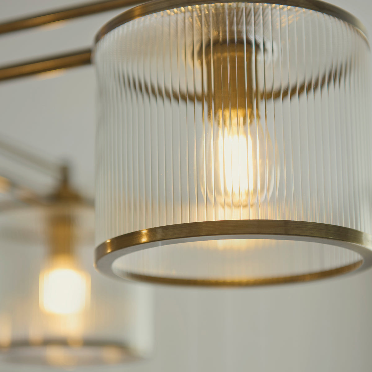 Detail of a Ridgeton ribbed glass shade with warm filament bulb and brushed brass trim
