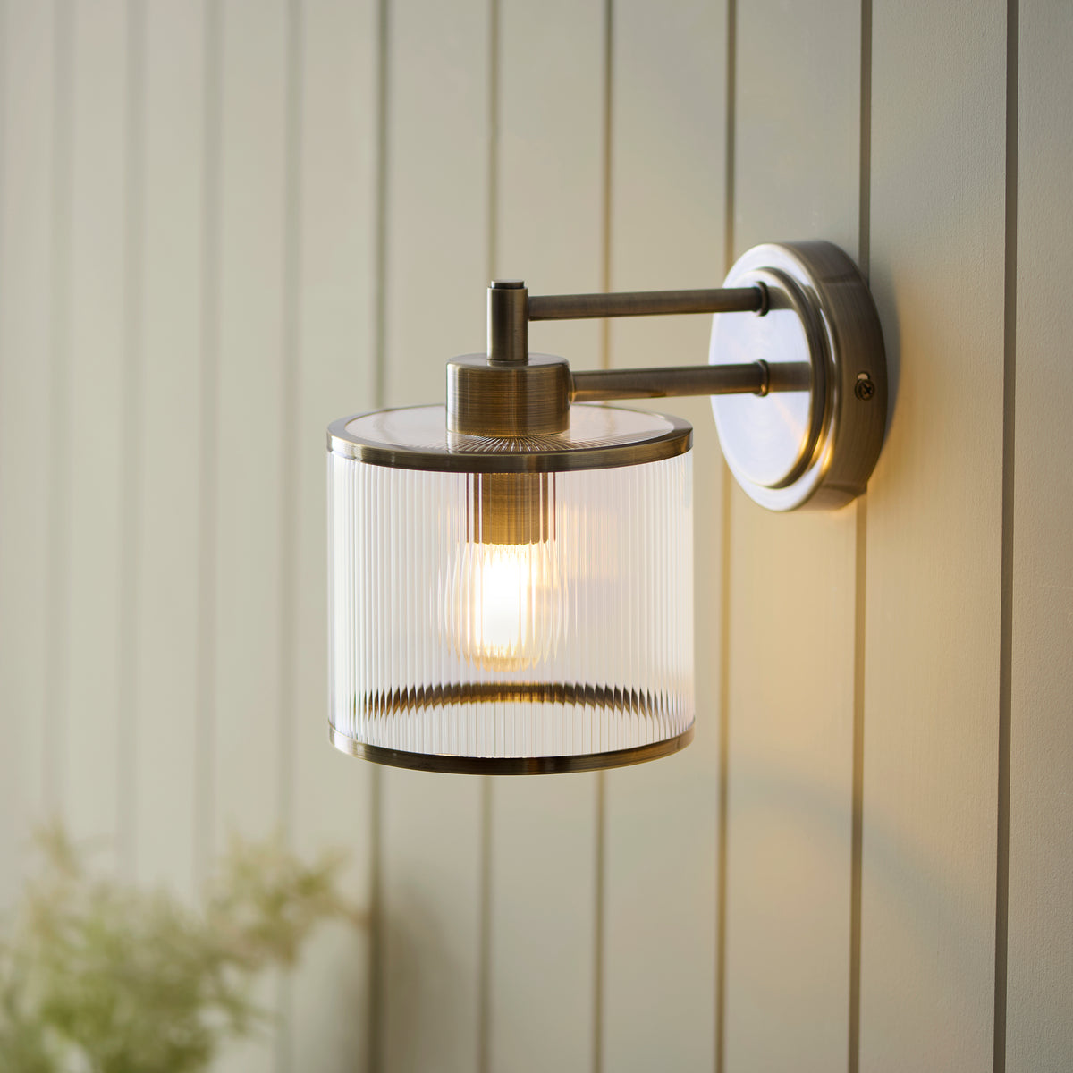 Ridgeton antique brass wall light glowing against cream tongue-and-groove panelling