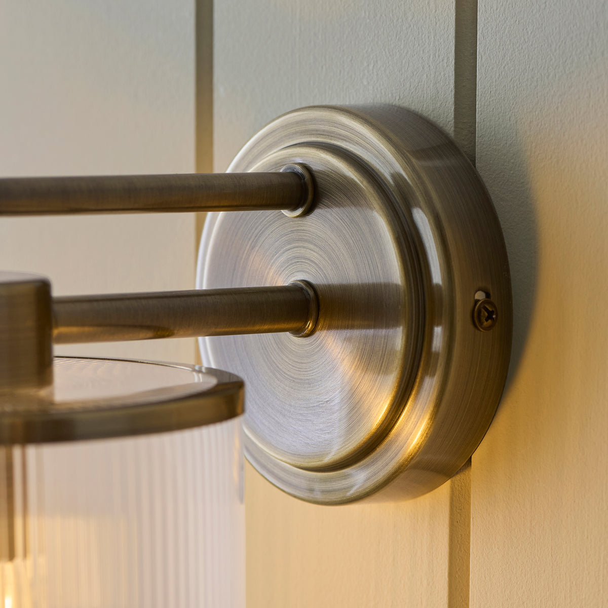Close-up of the Ridgeton wall light's round antique brass backplate and twin arms