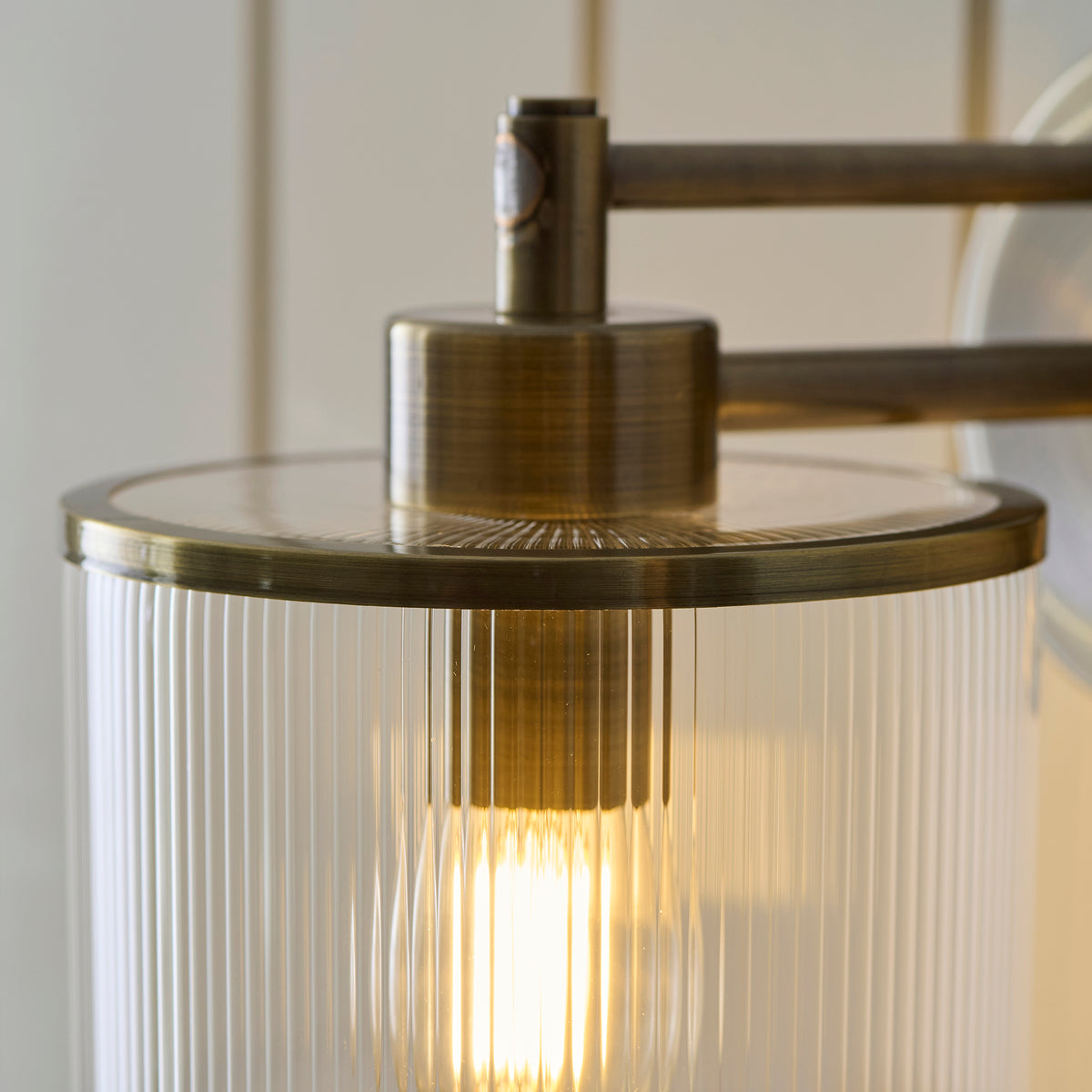 Detail of the Ridgeton ribbed glass shade with brass rim and lit filament bulb inside