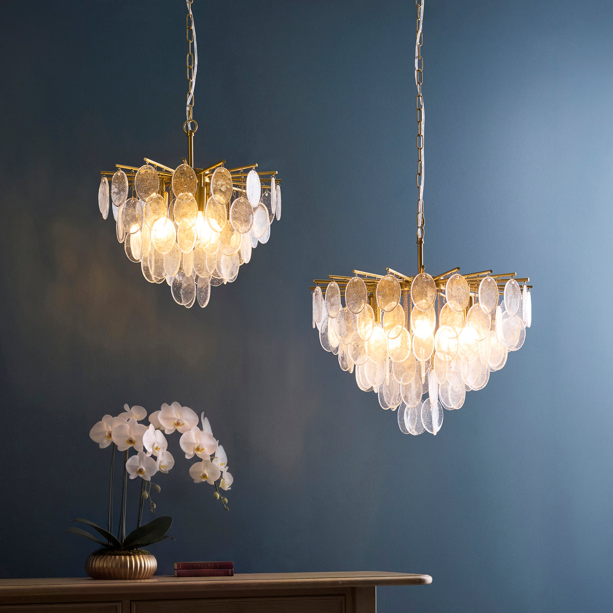 Two lit Loretta bubble glass pendants against dark teal walls above a sideboard with orchids
