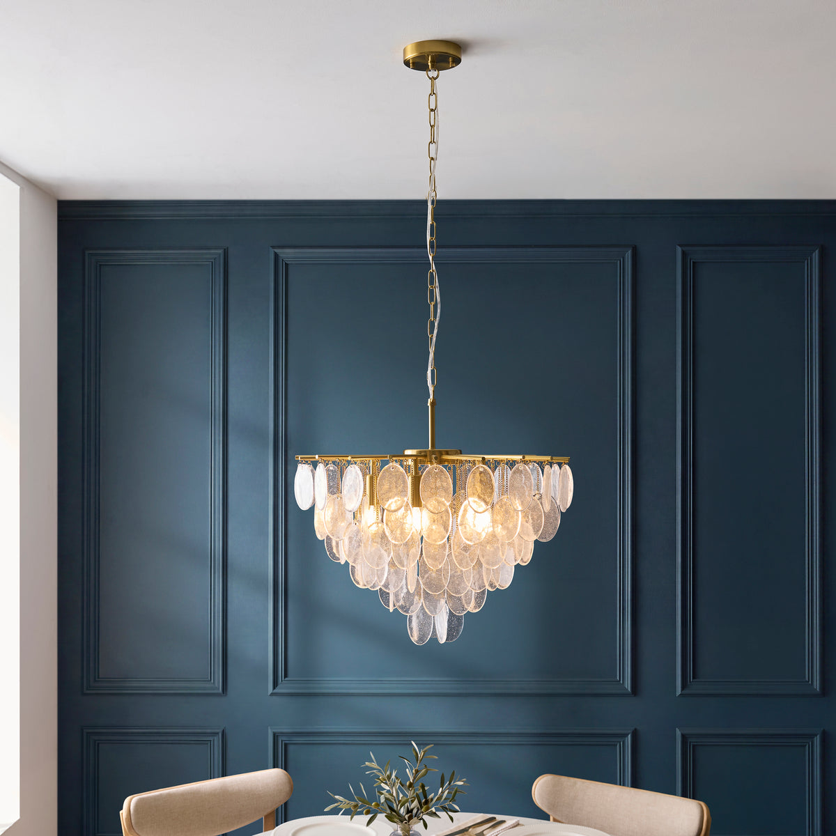 Loretta aged brass chandelier lit above a dining table in a navy panelled dining room