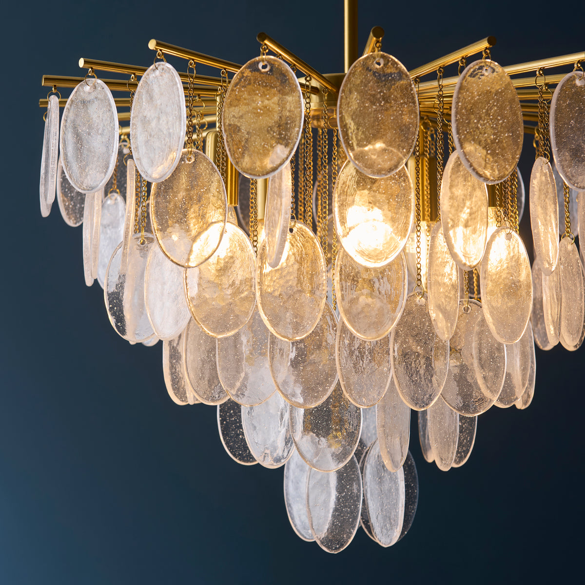 Close view of the Loretta chandelier's brass spokes and overlapping textured glass discs