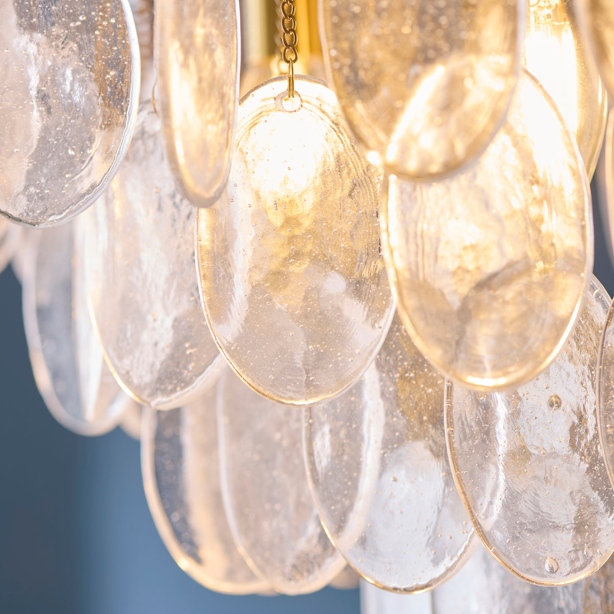 Detail of warmly lit clear bubble glass discs hanging from fine brass chains on the Loretta chandelier