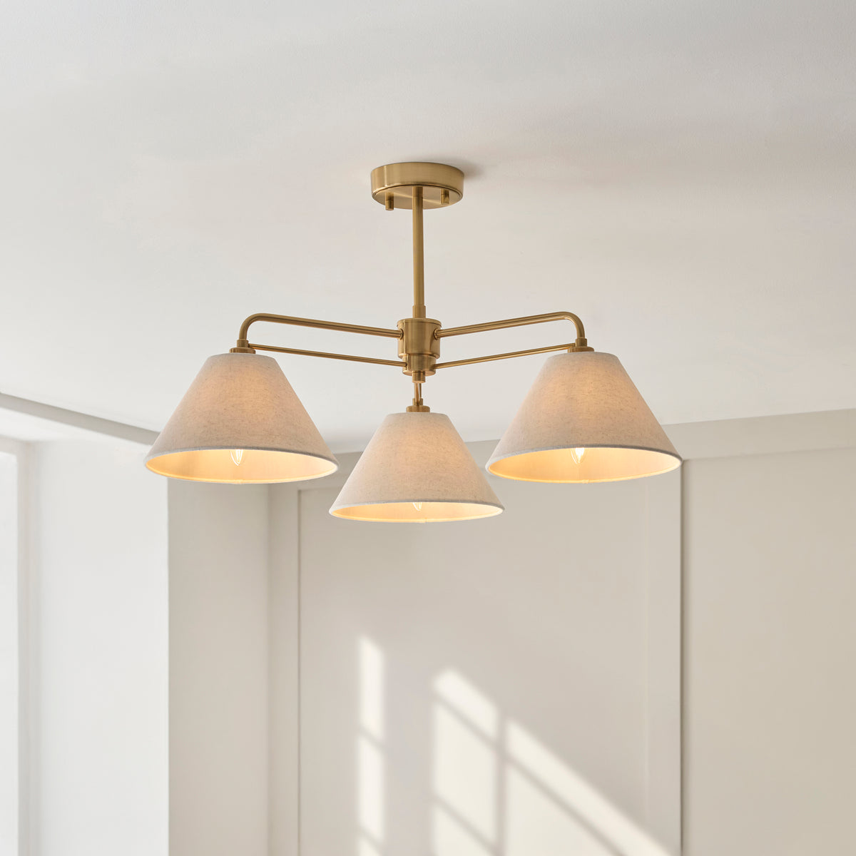 Lit Wallbridge semi flush light with brass arms and coned linen shades in a bright panelled room
