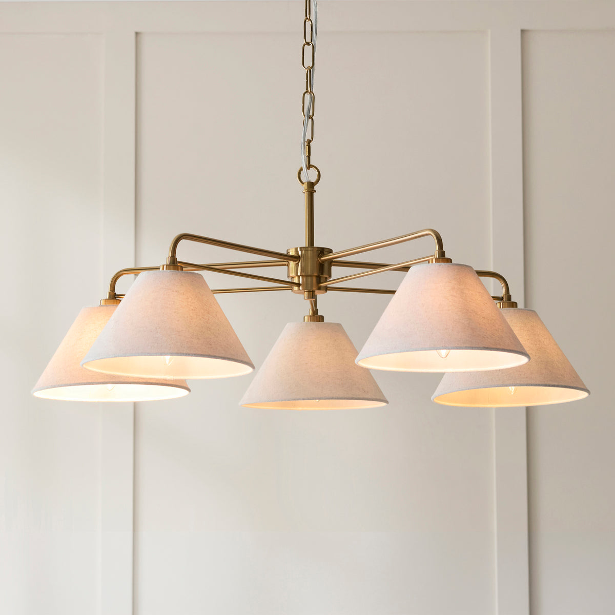 Angled view of the Wallbridge pendant's brass arms and glowing coned linen shades