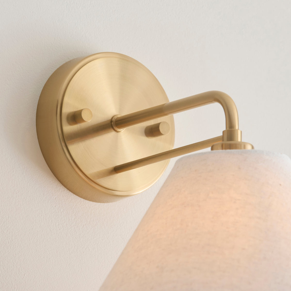 Detail of the Wallbridge wall light's round brushed brass backplate and swing arm