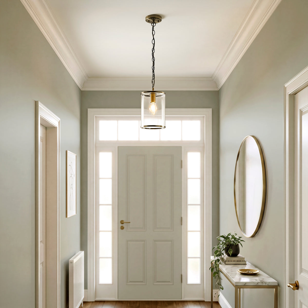 Hebden brass pendant with clear glass cylinder and lit globe bulb against a warm grey wall