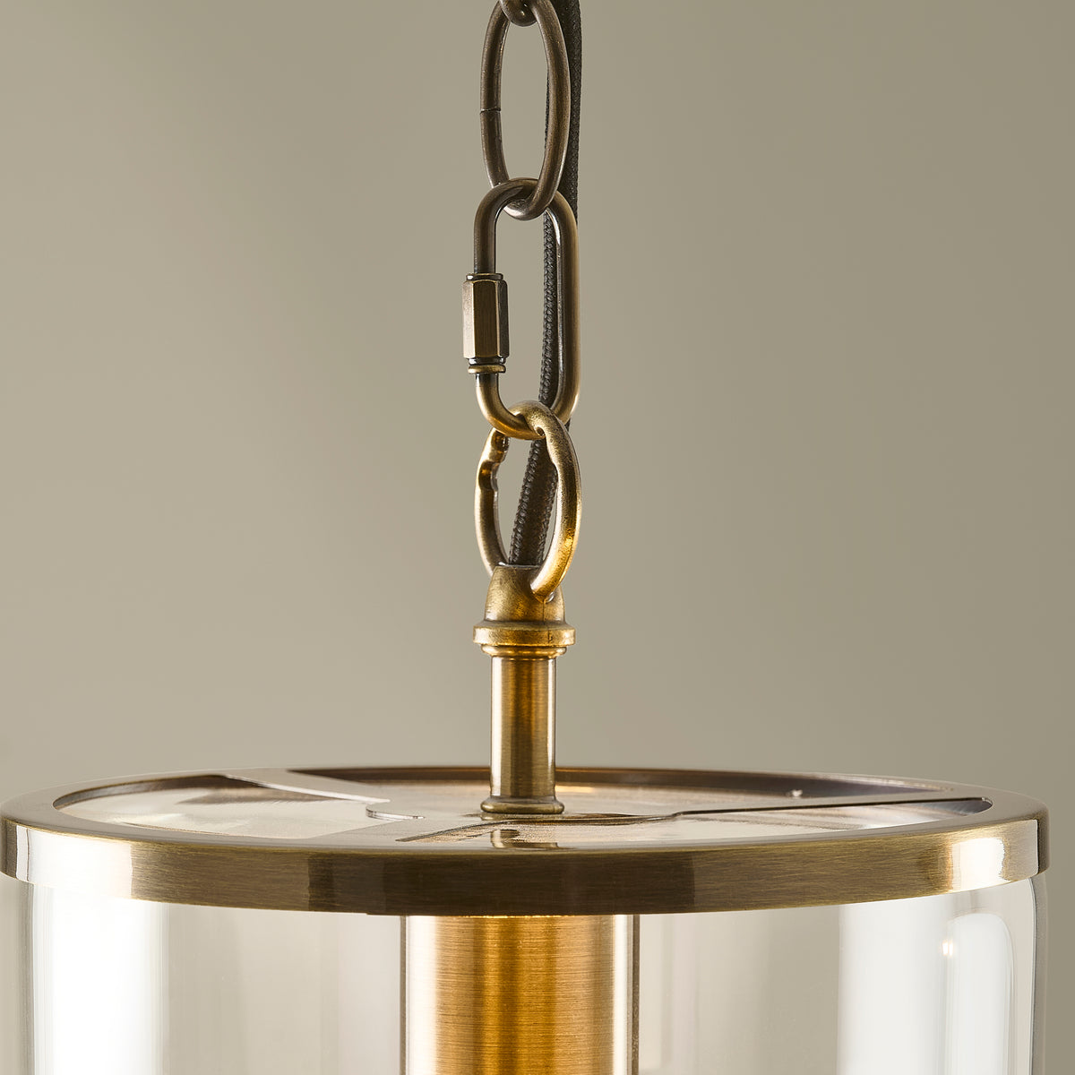 Hebden antique brass pendant lit with a filament bulb in its clear glass shade, on white