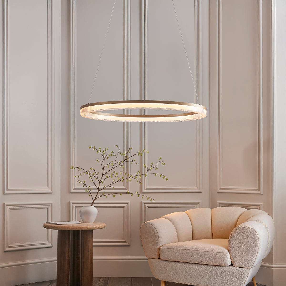 Lansina gold LED ring pendant glowing in a panelled living room with cream armchair and vase