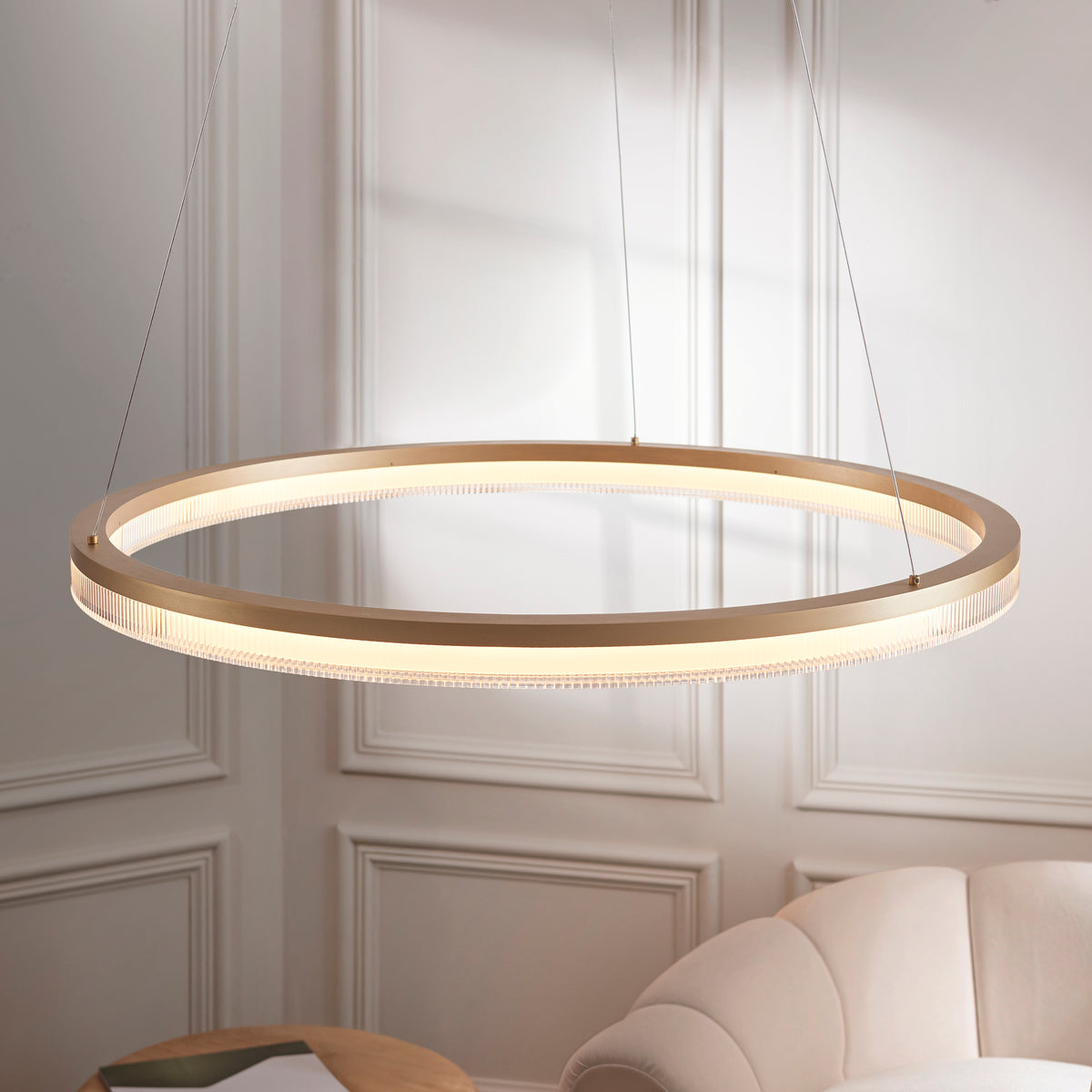 Lansina gold ring pendant seen at an angle, its ribbed LED diffuser glowing warmly