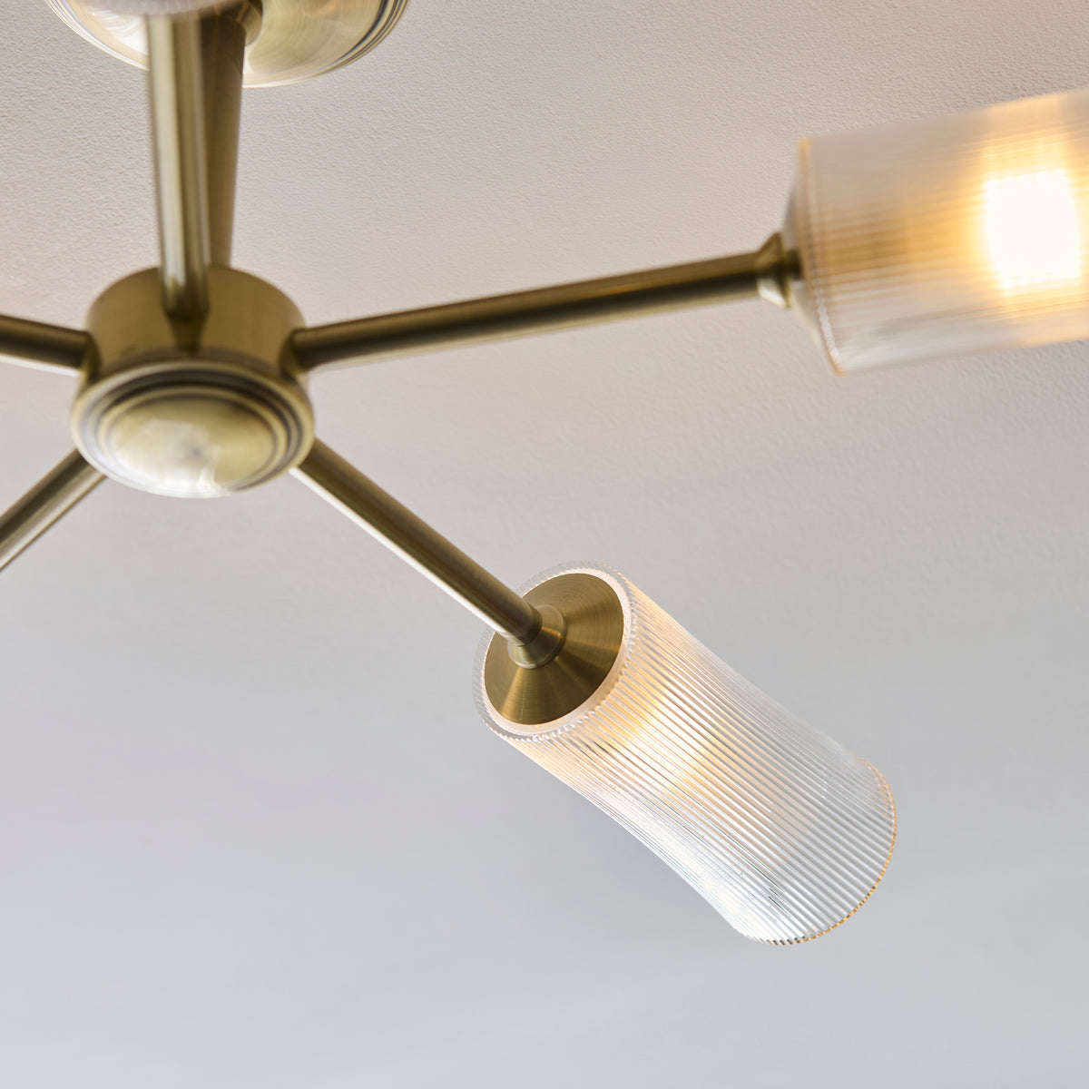Close-up of one Avelyn brass arm and its clear ribbed glass shade