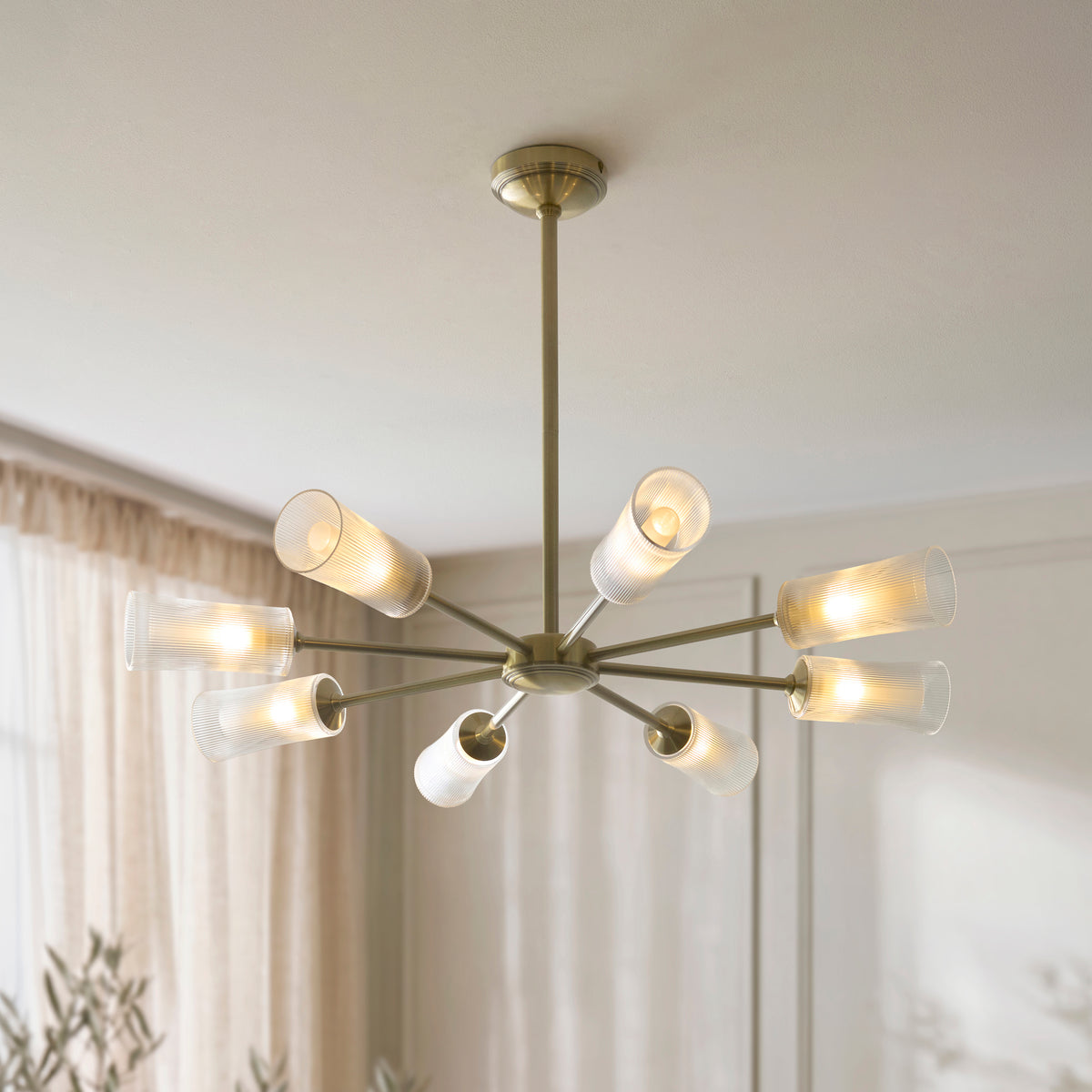 Avelyn brass chandelier with ribbed glass shades glowing beside pale curtains