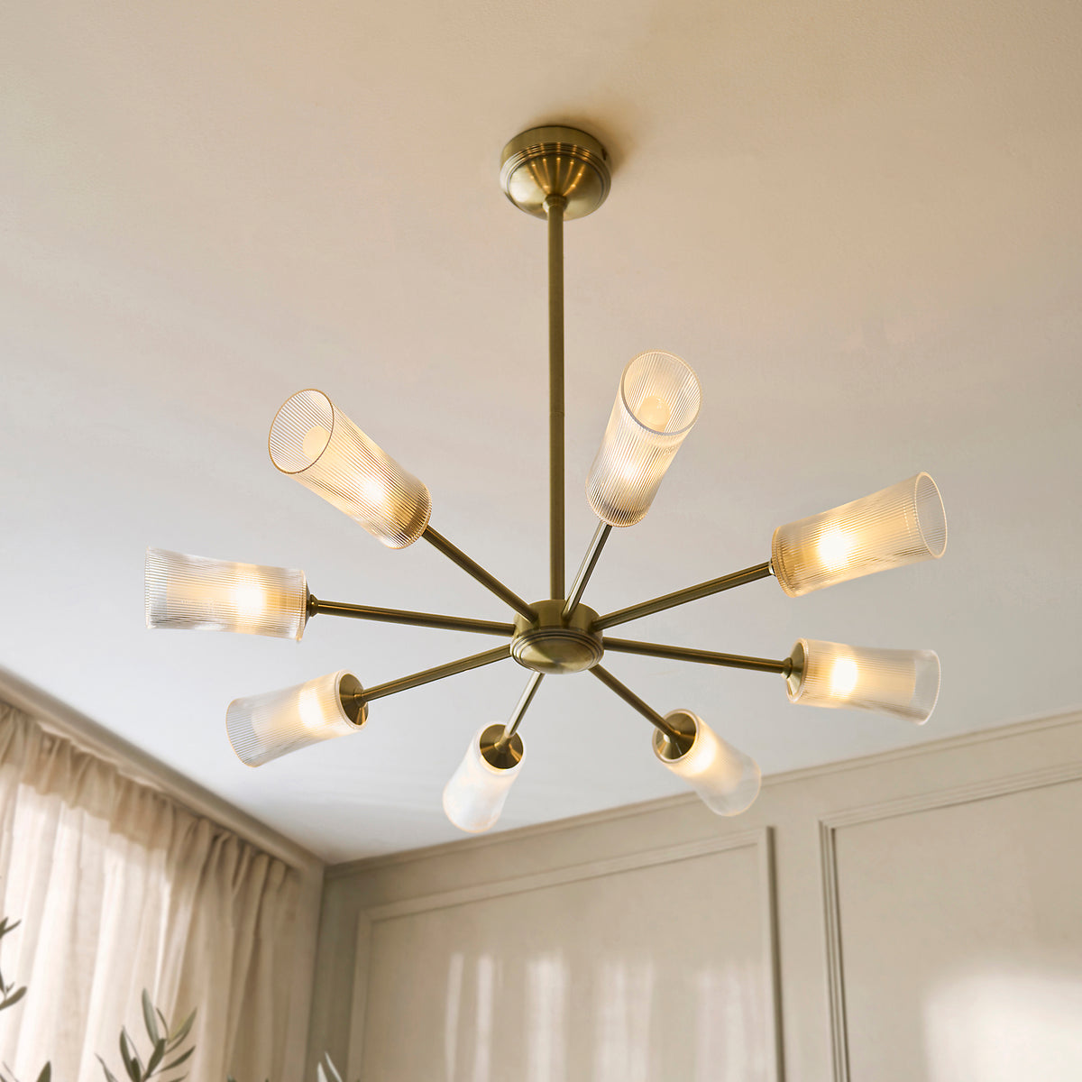 Avelyn chandelier seen from below, brass arms holding lit ribbed glass shades